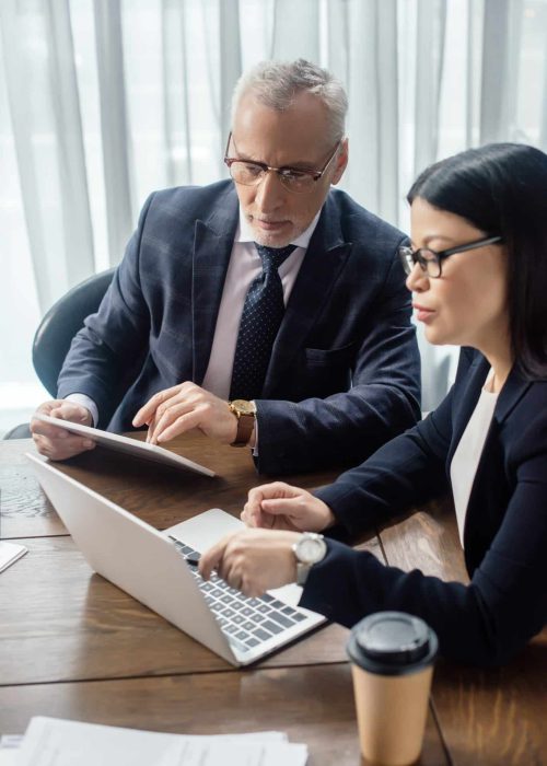 businessman and asian businesswoman looking at laptop and talking during business meeting